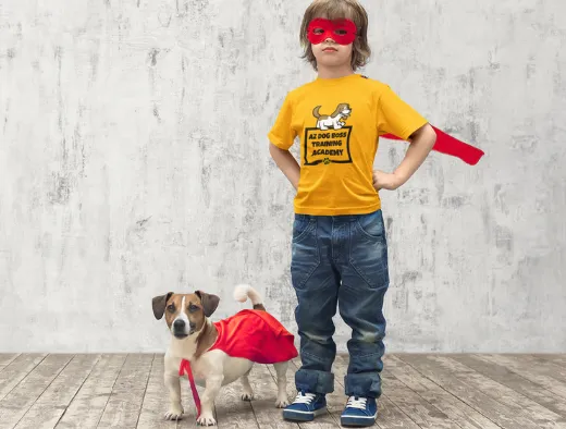 Young boy in an AZ Dog Boss Training Academy shirt with a small dog in a red cape